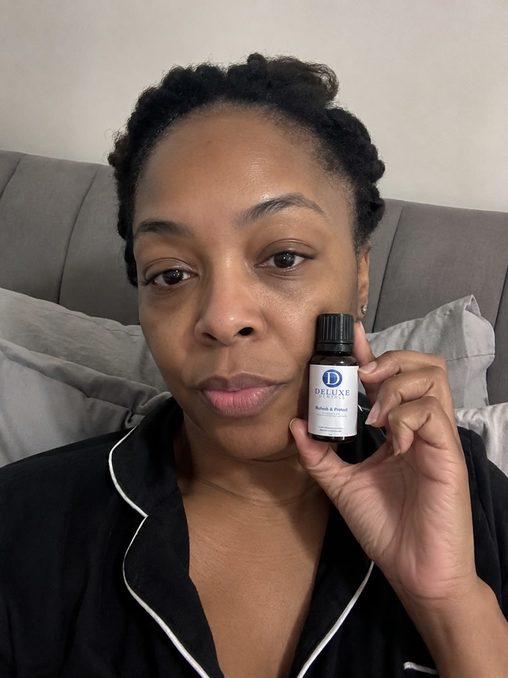 Customer holding the Refresh & Protect bottle beside her face in bed.