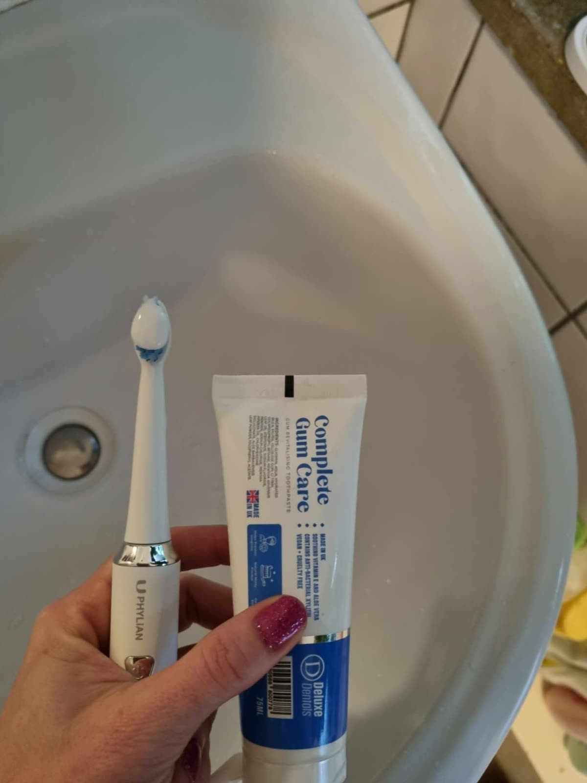 Customer holding the Complete Gum Care toothpaste tube with an electric toothbrush.